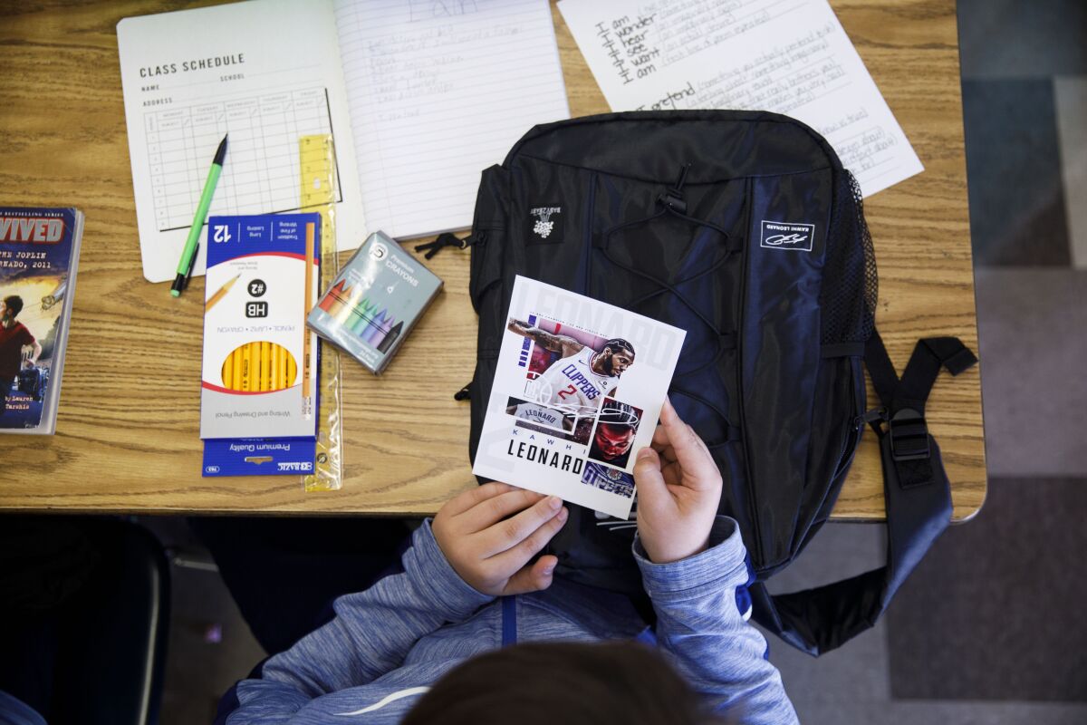 A student looks at a card of Clippers Kawhi Leonard after he gave backpacks away to students at One Hundred Seventh Street Elementary School on Tuesday in the Watts neighborhood of Los Angeles.