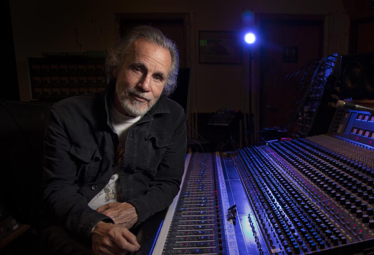 A man with gray hair and beard next to a mixing console