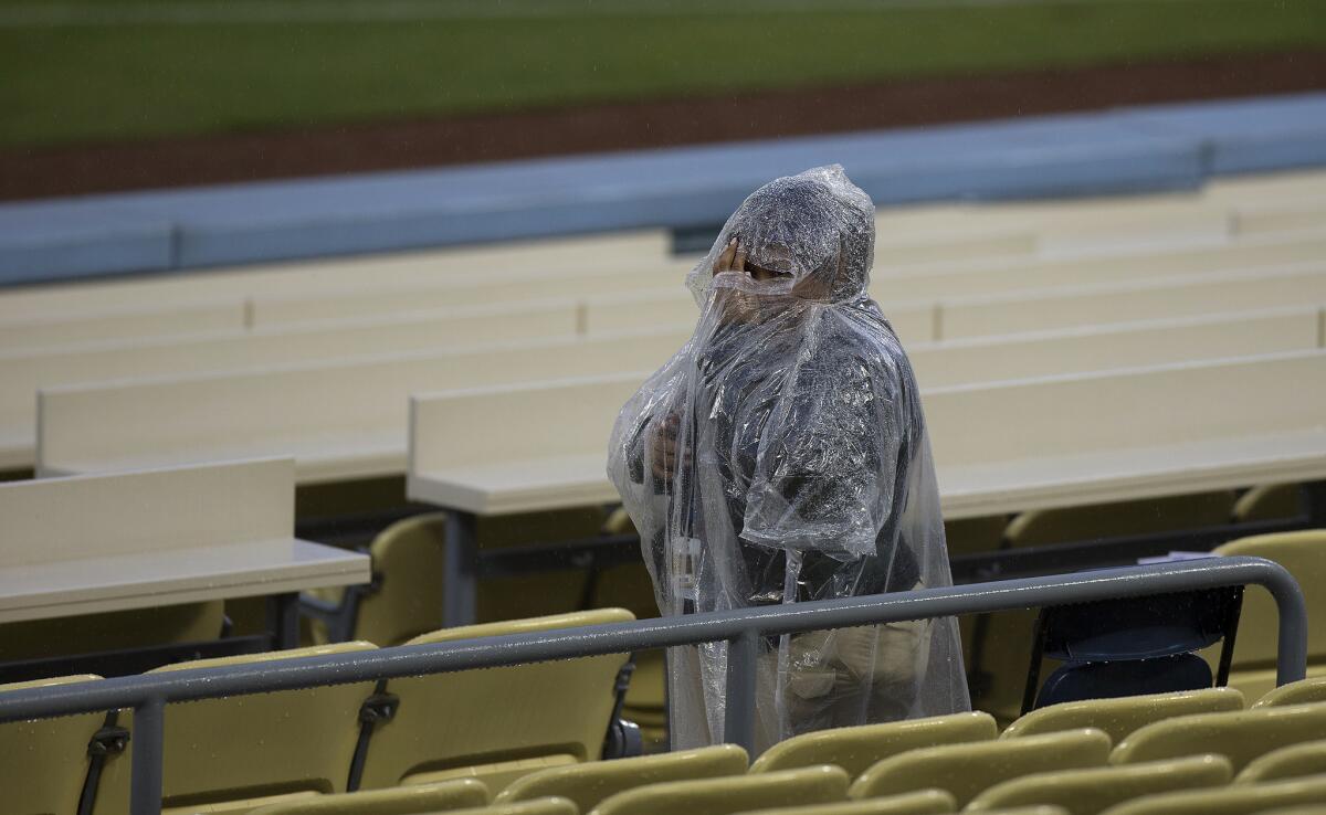An usher covers her face with a poncho as a spring rainstorm delays the start of the game between the Los Angeles Dodgers and San Diego Padres at Dodger Stadium on Tuesday.