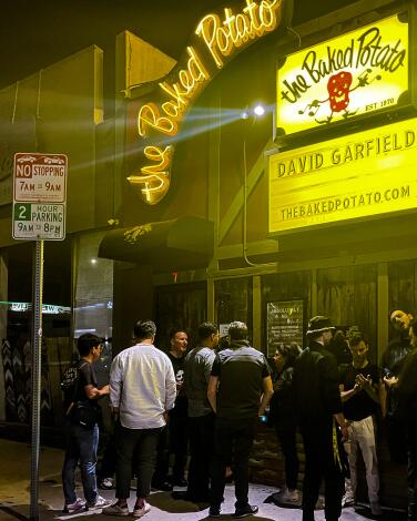 People stand outside the Baked Potato jazz club in Studio City under its yellow signs.