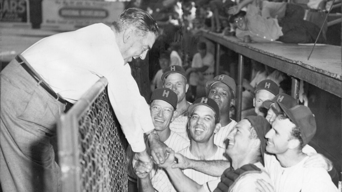 Hollywood Stars co-owner Bob Cobb leans over dugout fence to congratulate players in 1953.