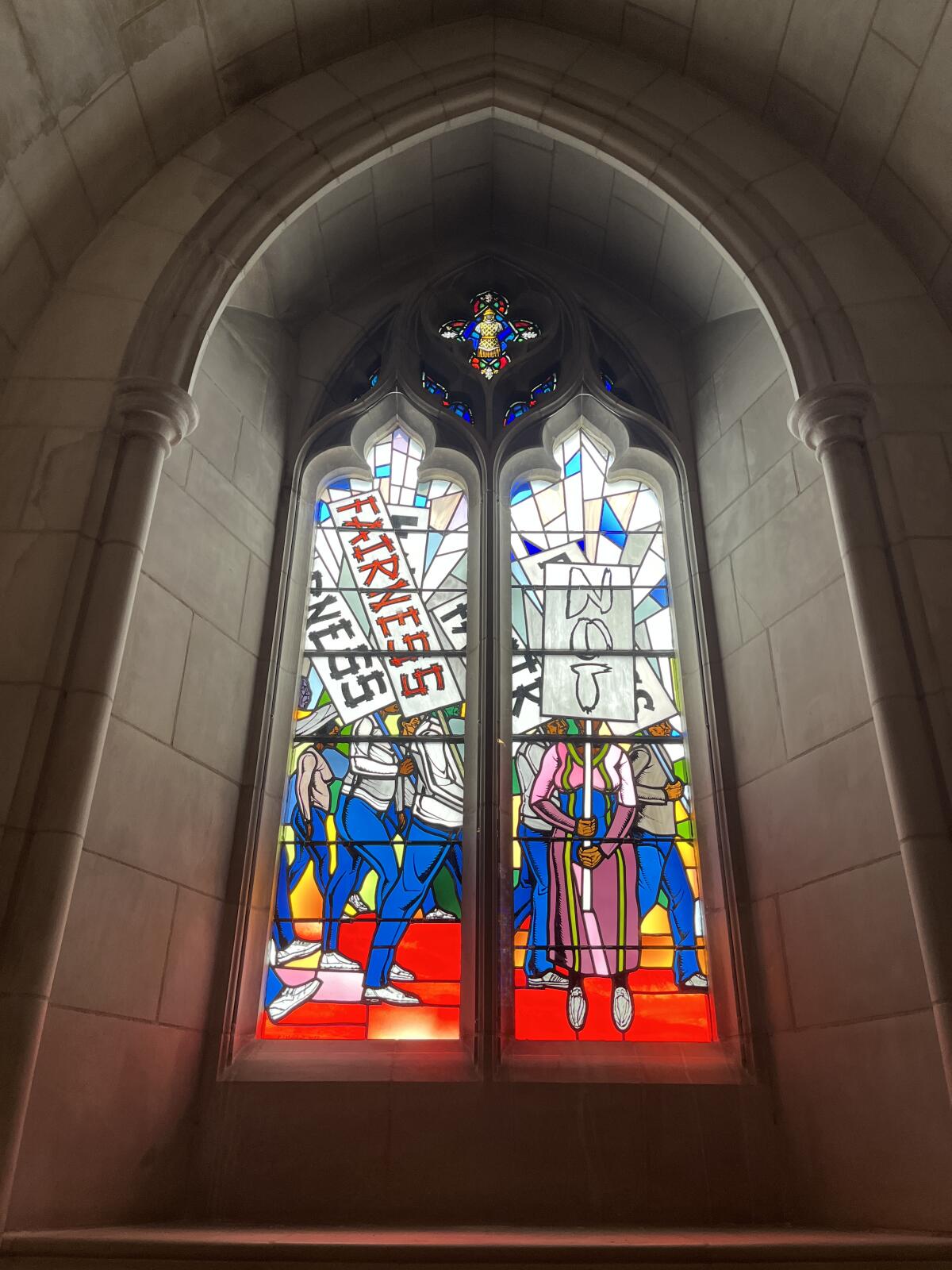 A view of two lancet-shaped stained glass windows show Black protestors bearing signs that read "FAIRNESS" and "NOT."