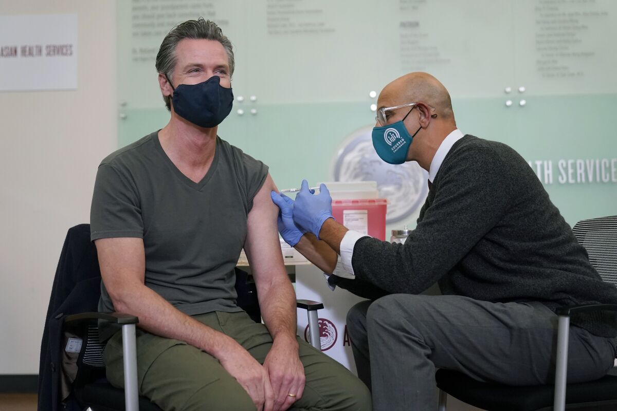 FILE — California Gov. Gavin Newsom, left, receives a Moderna COVID-19 vaccine booster shot from California Health and Human Services Secretary Dr. Mark Ghaly at Asian Health Services in Oakland, Calif., Wednesday, Oct. 27, 2021. After abruptly canceling his plans last week to attend the United Nations climate summit in Scotland, Newsom did not participate in the conference virtually the first week of November 2021 while attending to unspecified family obligations. (AP Photo/Jeff Chiu, File)