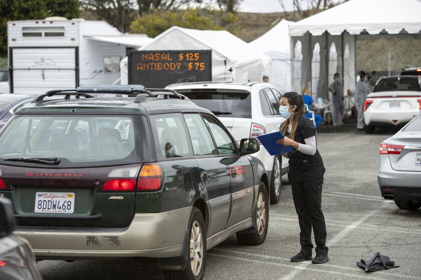 A Healthcare professional helps a driver waiting in line for a COVID-19 test at a drive through testing site at the Westminster Mall on Tuesday, April 7.