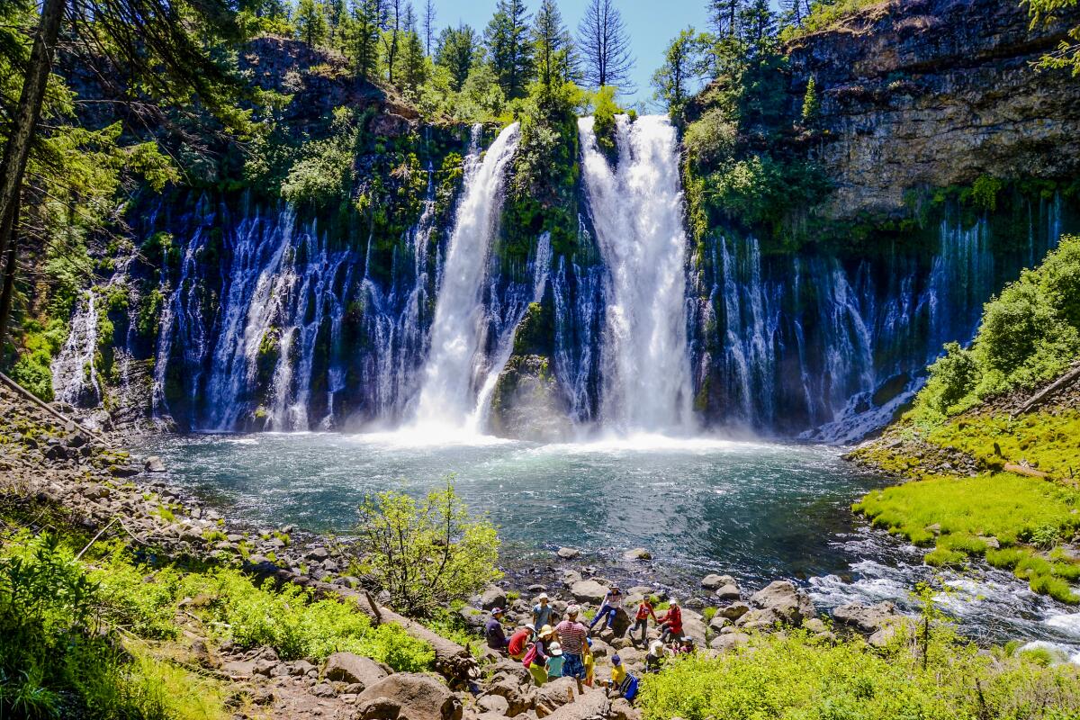 Waterfalls pour into a pool surrounded by greenery.