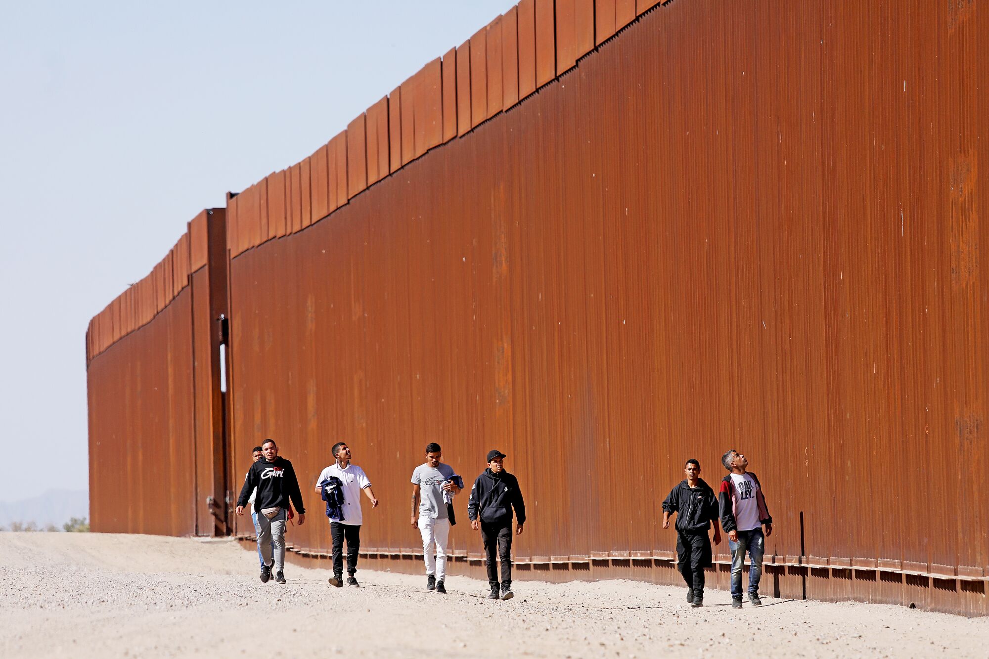 Immigrants walk along the border wall to turn themselves over to U.S Border Patrol agents in San Luis Rio Colorado, Mexico.