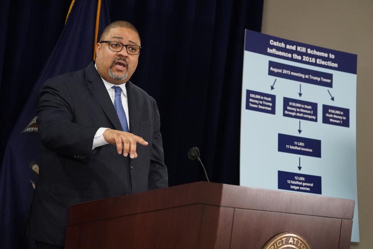 Manhattan District Attorney Alvin Bragg speaking and gesturing at a lectern by a chart.