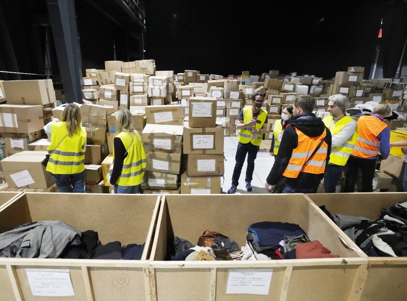 People wearing reflective vests stand near stacks of boxes and bins filled with clothing 