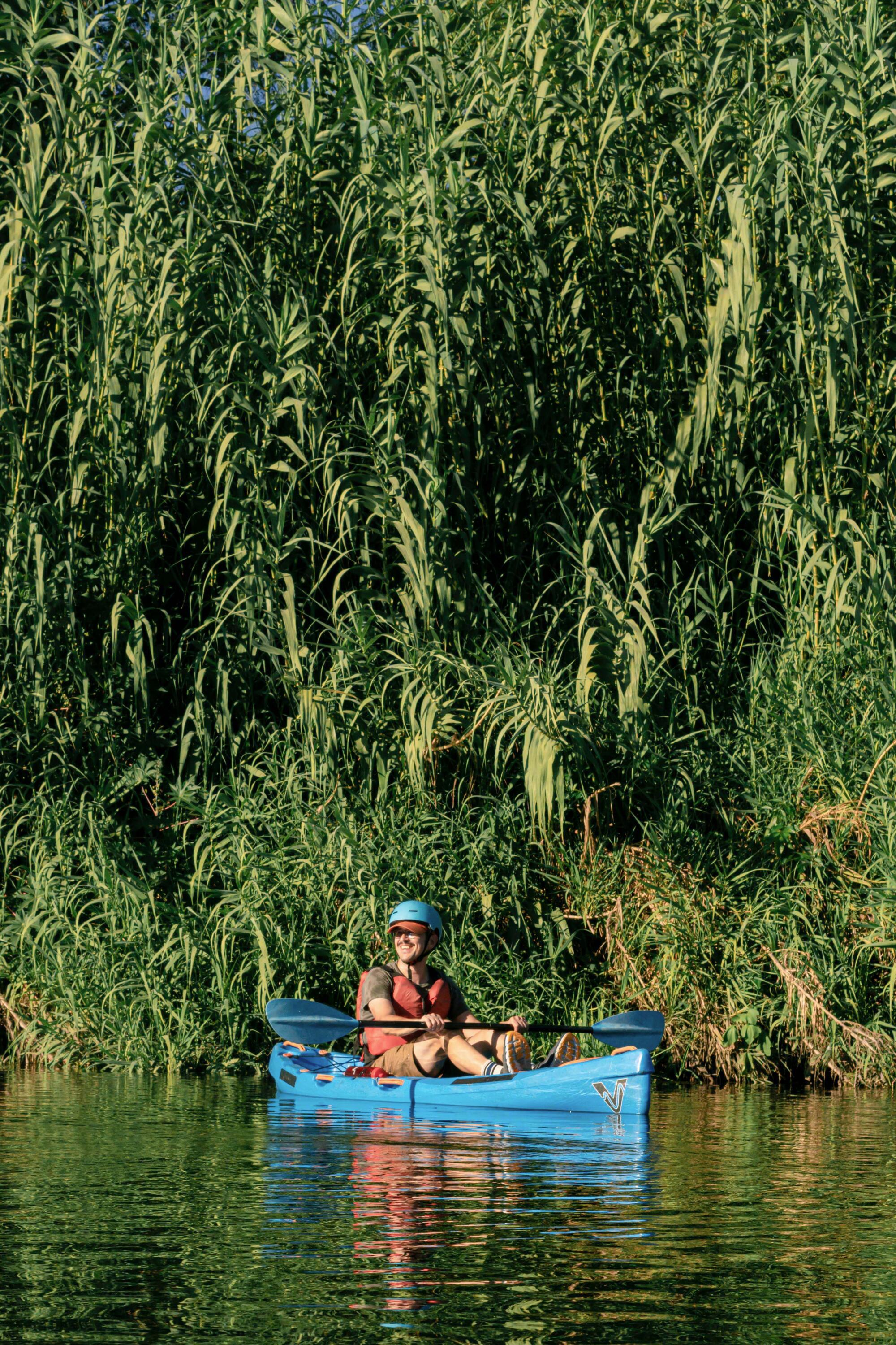A man sits in a kayak in front of some trees.