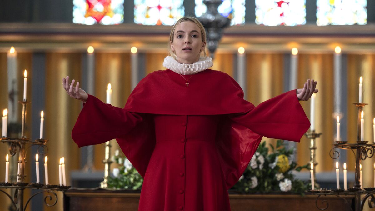 A woman wearing a crimson cassock with a white ruffled collar stands before an altar, hands upturned in a worshipful gesture