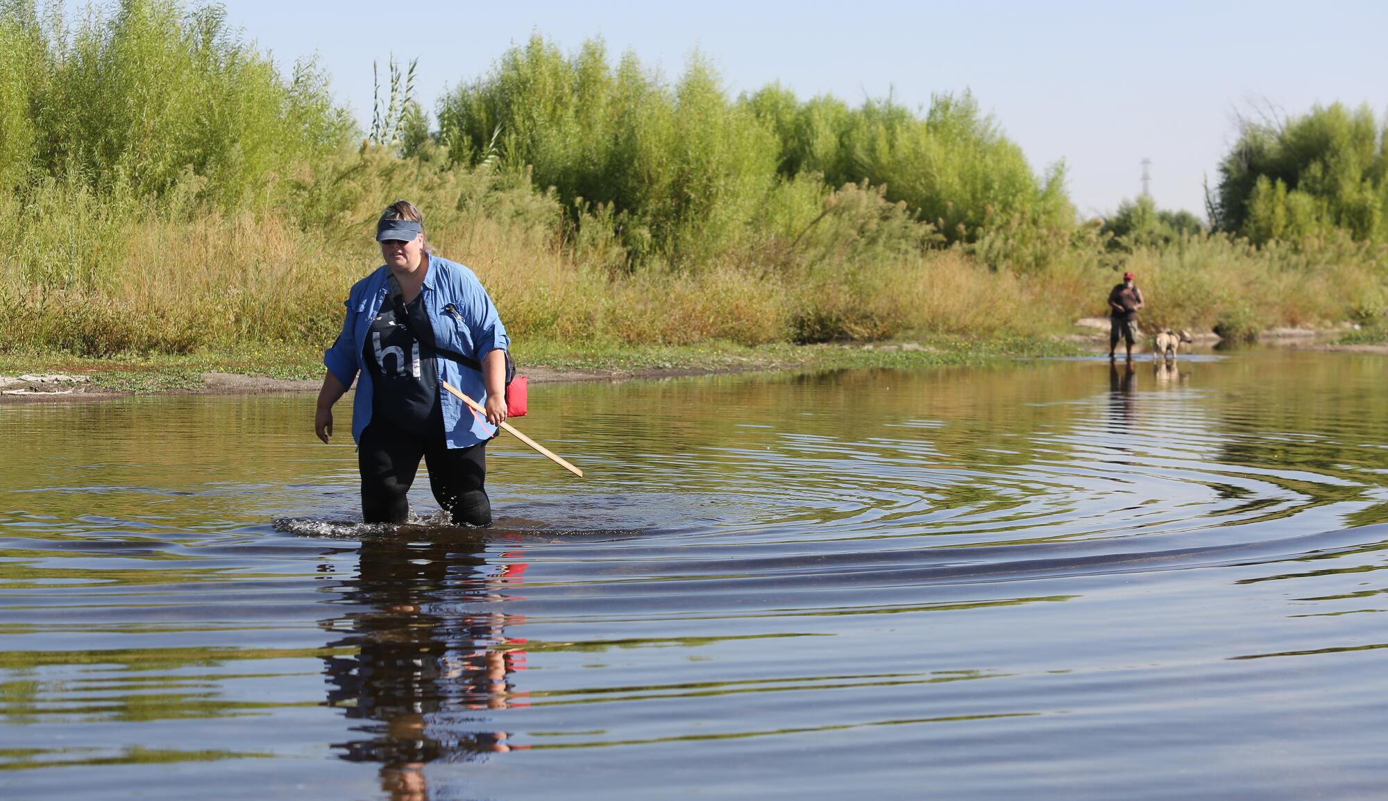 A woman wades through a shallow river.