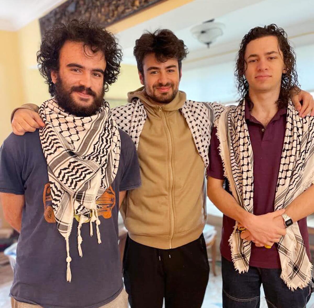 Three Palestinian college students smile wearing black and white keffiyehs.