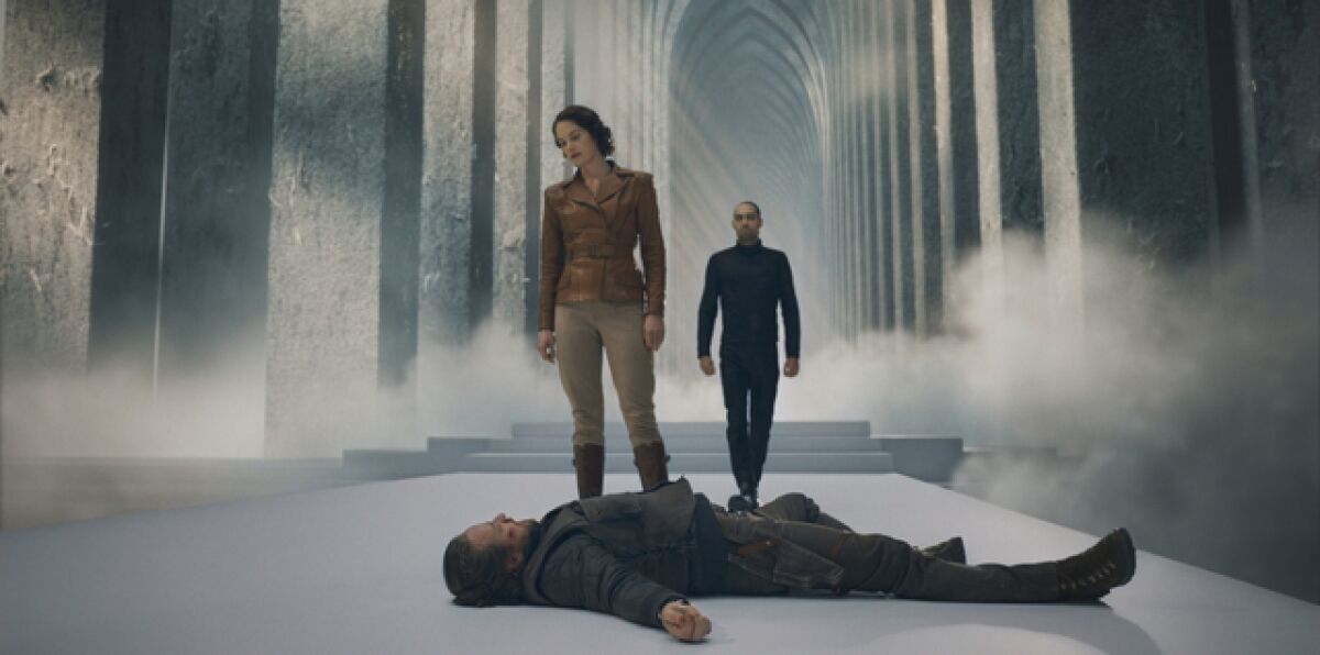 Two people standing over a body in an airy hallway