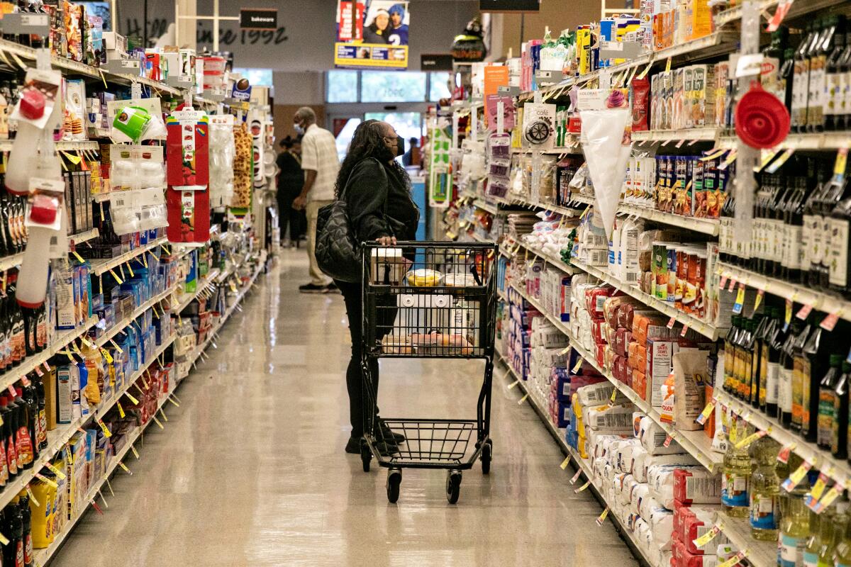 A shopper with a cart looks at grocery items.