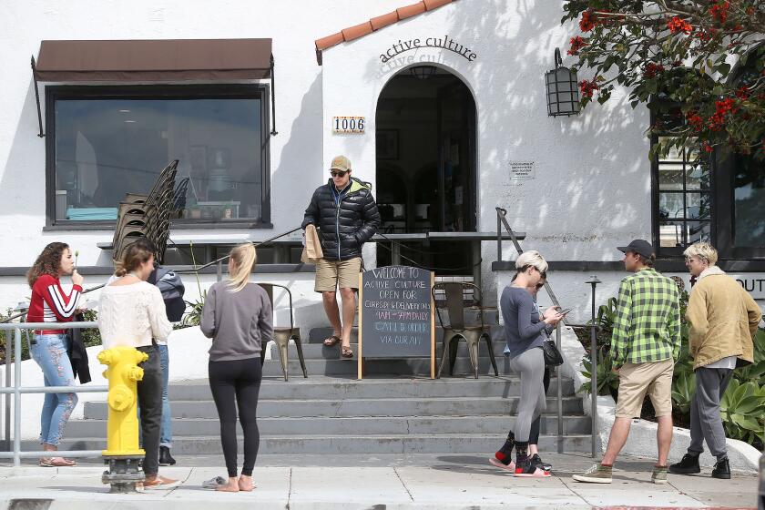 Small groups wait on the sidewalk for phone in, pick-up orders at Active Culture in Laguna Beach as local businesses are being asked to avoid small gathering and uphold social distances during the widening Coronavirus pandemic.