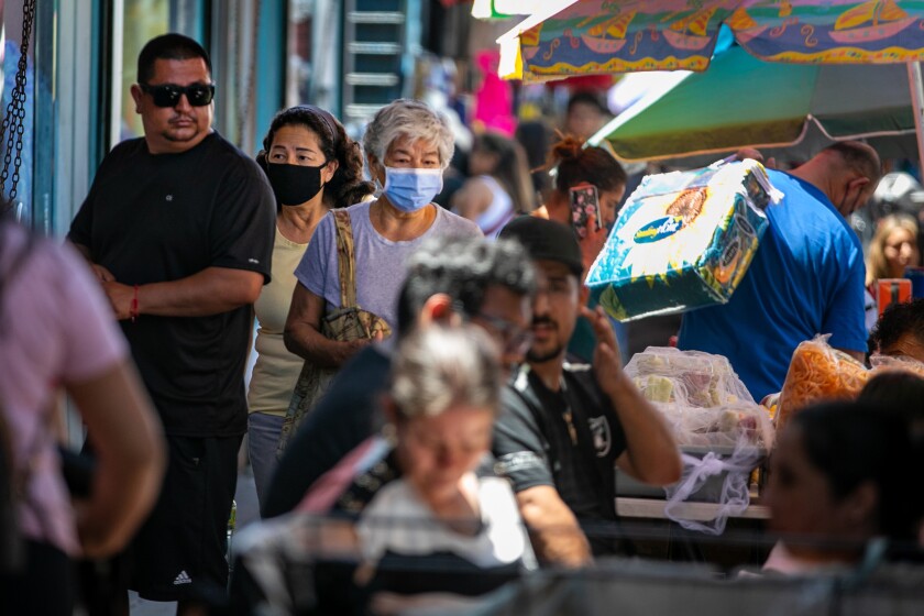 People shop and work in a market, some wearing masks