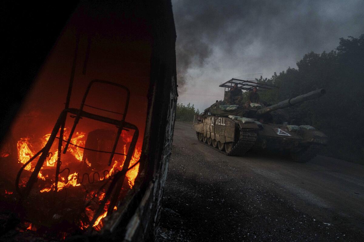 A tank passes by a burning car.