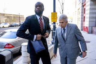 Pras is buttoning his dark blue suit as he looks away in front of car next to David Kenner who is in a gray suit