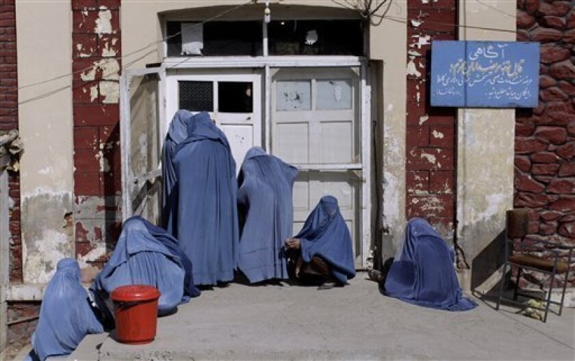 FILE - In this Wednesday, Oct. 26, 2011 file photo, an Afghan woman, center, peeks inside a hospital while she and others wait for an employee to let them enter, on the outskirts of Kabul, Afghanistan. An Afghan woman has been strangled to death, apparently by her husband, who was upset that she gave birth to a second daughter rather than the son he wanted, police said Monday. It was the latest in a series of grisly examples of subjugation of women that have made headlines in Afghanistan in the past few months including a 15-year-old tortured and forced into prostitution by in-laws and a female rape victim who was imprisoned for adultery. (AP Photo/Muhammed Muheisen, File)