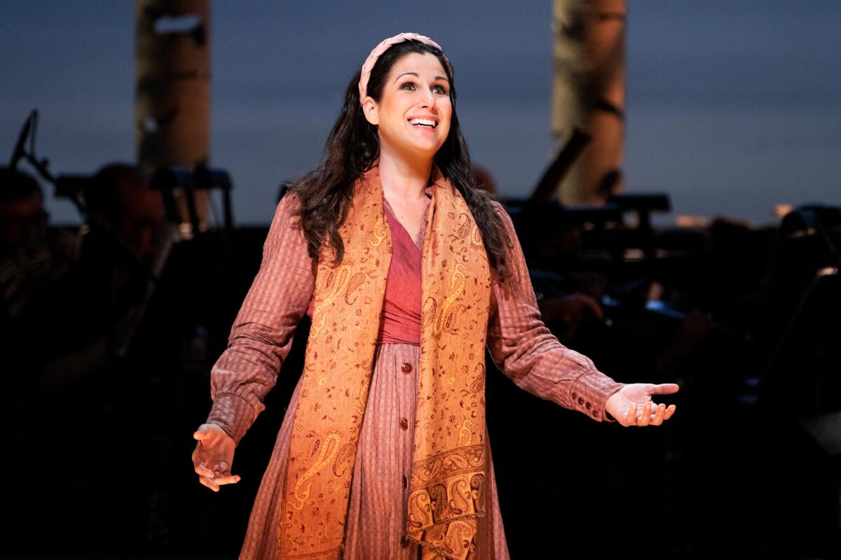 A woman in colorful storybook clothing performs in front of an orchestra.