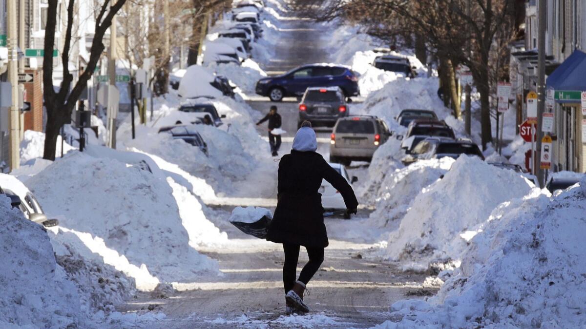 A woman carries a shovel-full of snow down the street to a pile while digging her car out in Boston on Jan. 5, 2018.