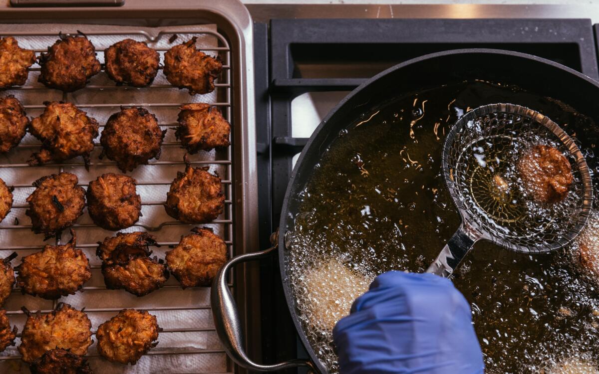 Fried latkes sit on a cooling rack as other latkes are fried.