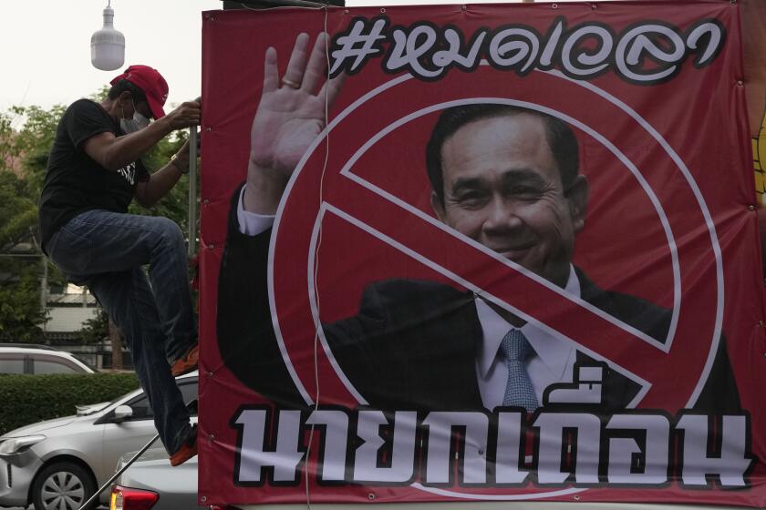 An anti-government protester climb on car beside a poster of Prime Minister Prayuth Chan-ocha in Bangkok, Thailand, Wednesday, Aug. 24, 2022. Thailand's Constitutional Court ruled Wednesday that Prime Minister Prayuth Chan-ocha must suspend his active duties while the court decides whether he has overstayed his legal term in office. The poster reads "Time is over." (AP Photo/Sakchai Lalit)