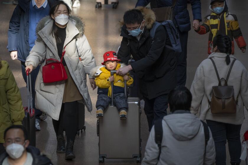 Un hombre empuja una maleta con un niño montada en ella en la estación oeste de trenes de Beijing, el miércoles 18 de enero de 2023. (AP Foto/Mark Schiefelbein)