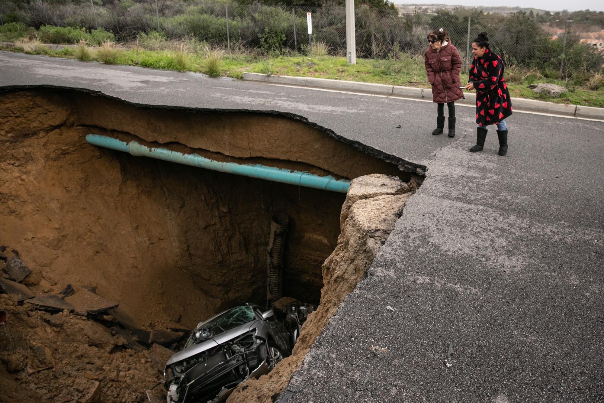 Two Chatsworth residents view the sinkhole that swallowed two cars on Iverson Road south of Zaltana Street