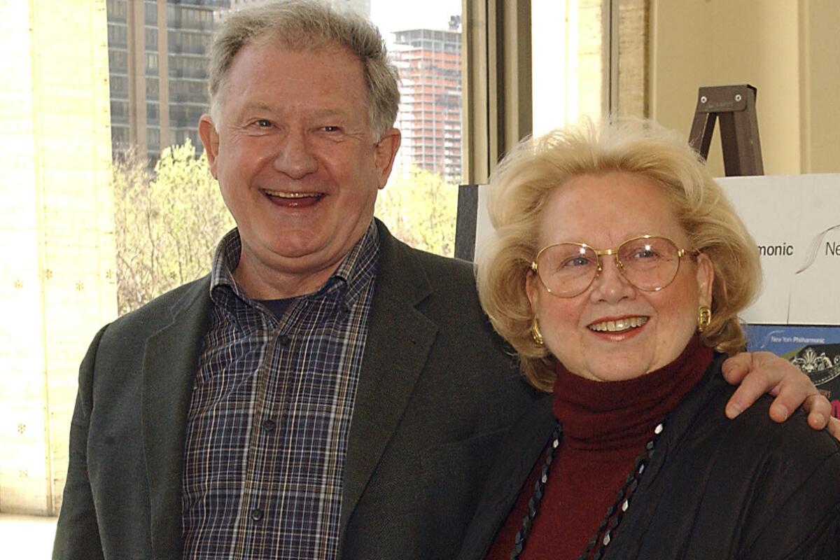 A man in a plaid shirt and sports coat with arm around a woman.