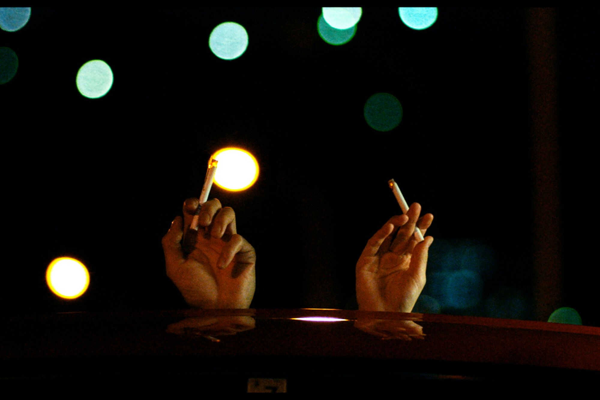 Two hands holding cigarettes stick up through a car's sunroof in a scene from "Drive My Car."
