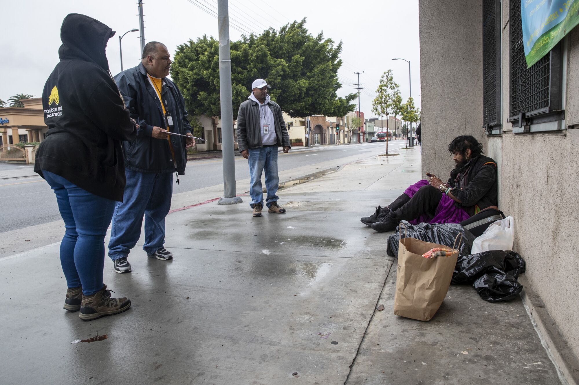 HOPICS outreach nurse Kenya Smith, right, Ralph Gomez, center, and Kat Johnson, left, leave a bag of food for Davis Soto, taking care to stay at least six feet away from him. The coronavirus pandemic has led to a list of new precautions that outreach workers must follow.
