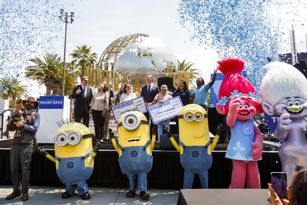 Gov. Gavin Newsom at a Universal Studios news conference with people in Minions and Trolls costumes in front of the stage. 