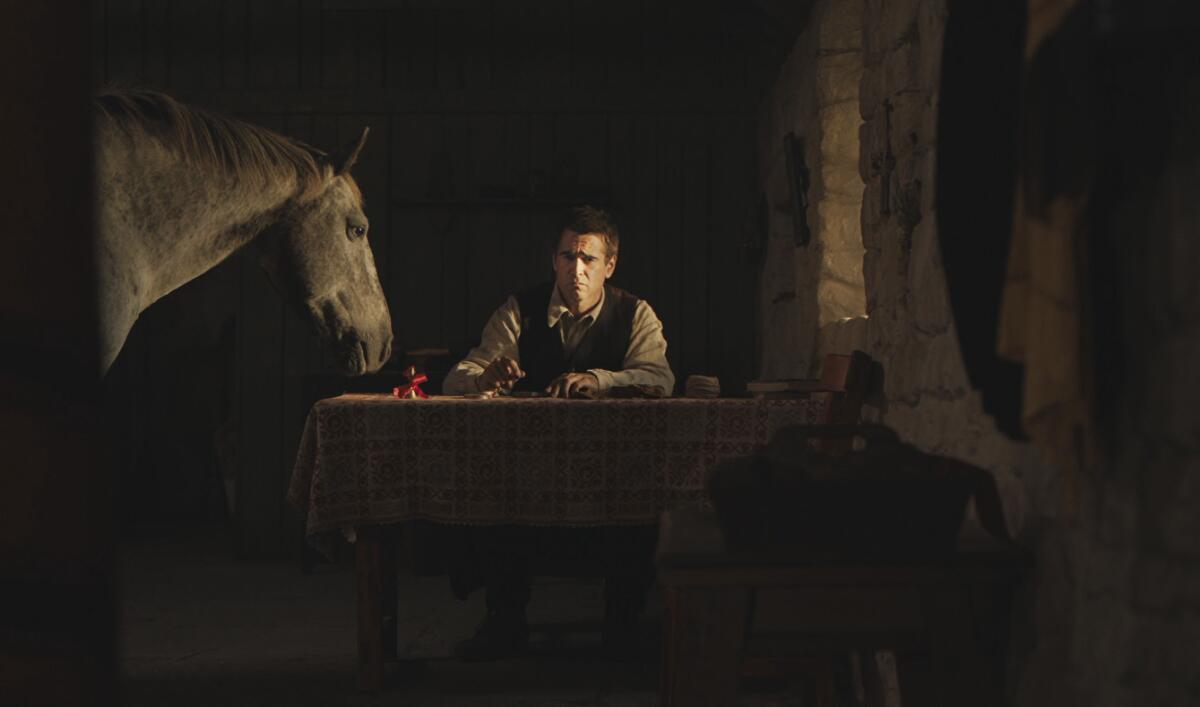 A man sits at a table in a darkened room, with a horse leaning over the table.