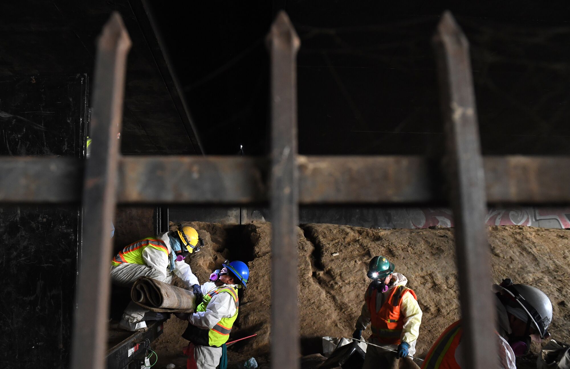 A cleanup crew is seen through wrought-iron gates along a freeway underpass.