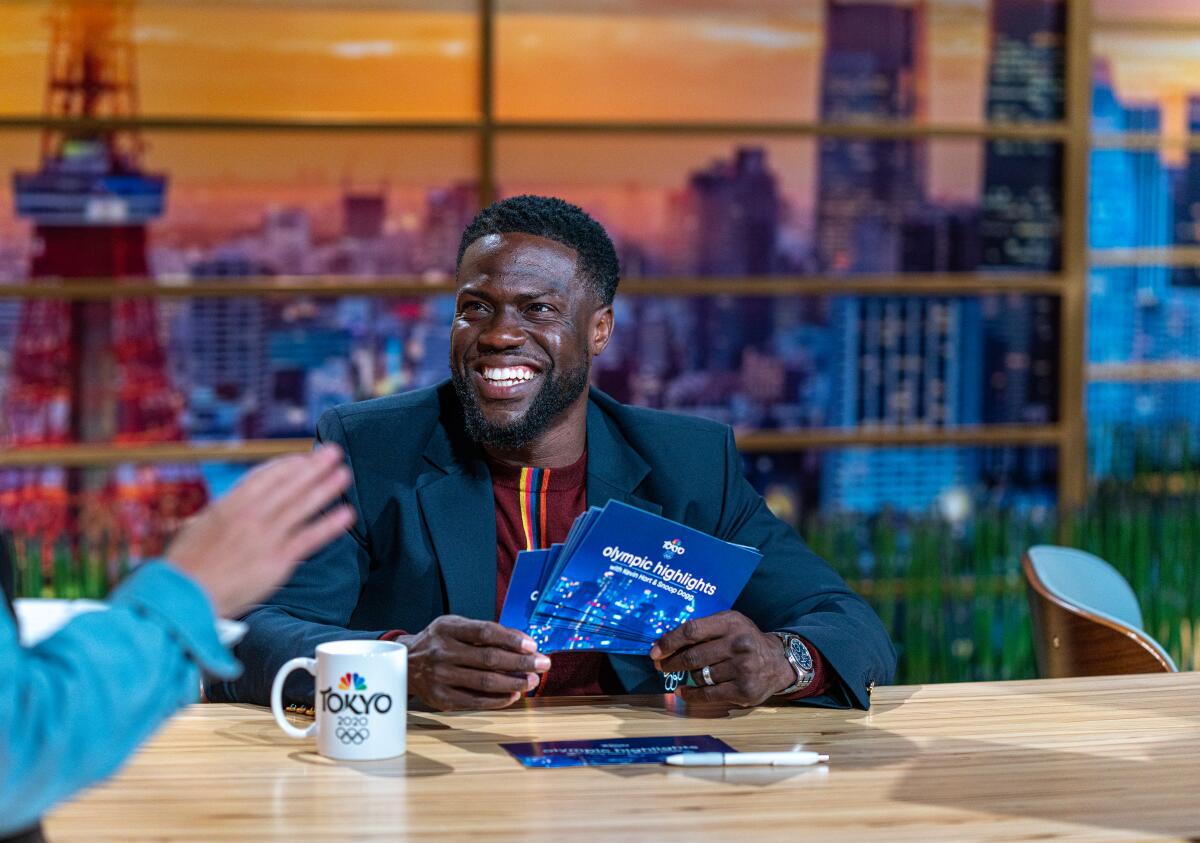 Kevin Hart tapes smiles while holding notecards that say "Olympic highlights" on the back.