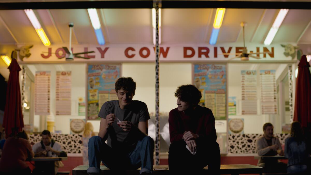 Fin Argus and Wyatt Olef sit on a table in front of a snack shop in the movie "Stay Awake."