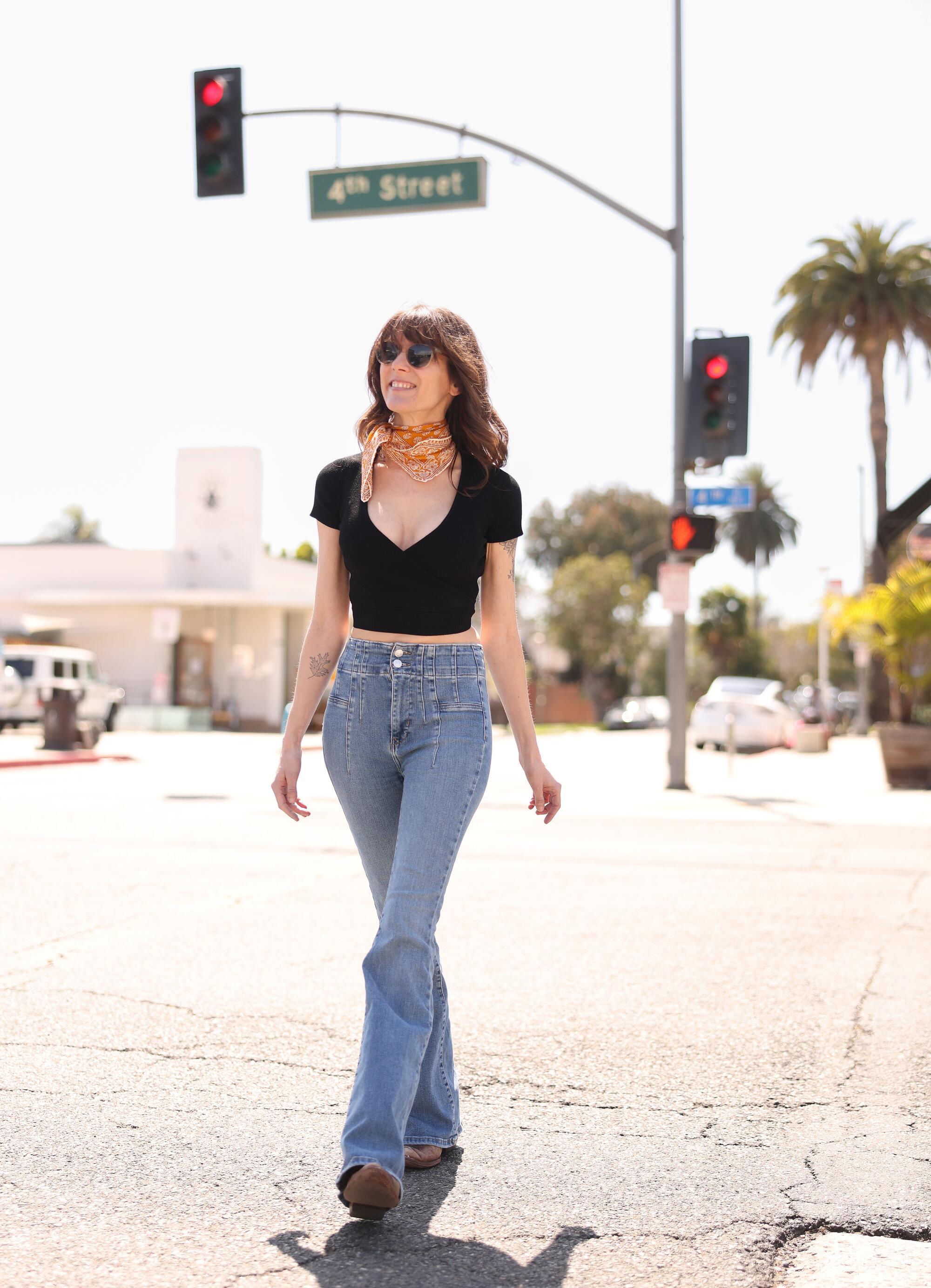Harrison crosses a street in jeans and a black top.