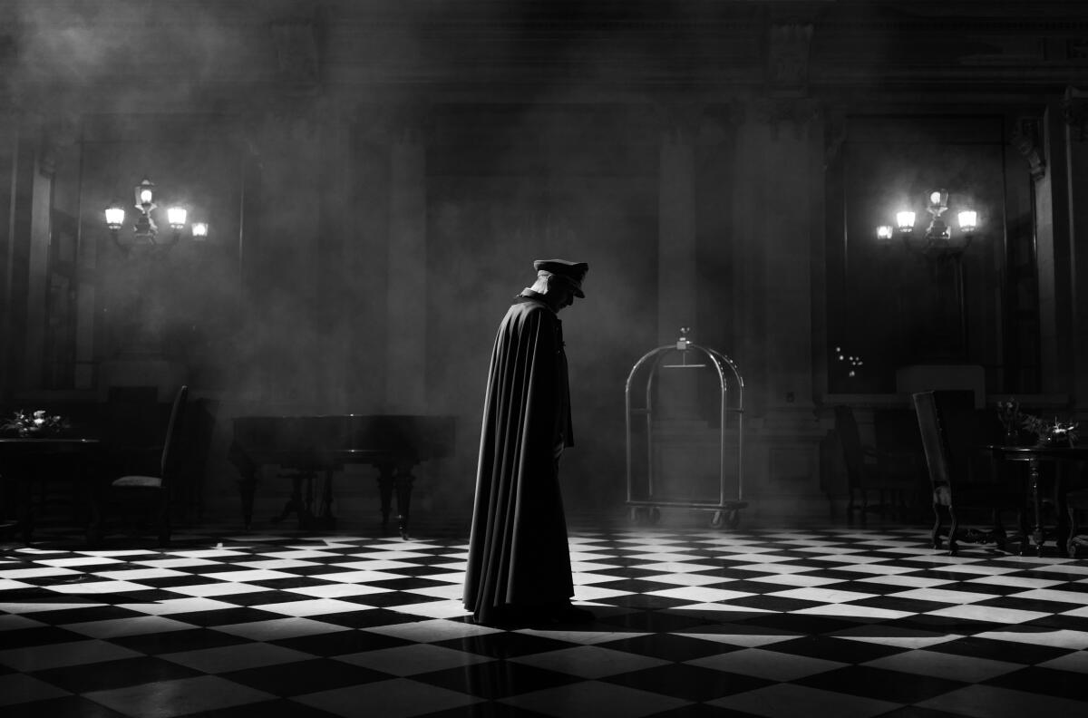 In a black-and-white film still, a caped vampire looms over a checkered floor.