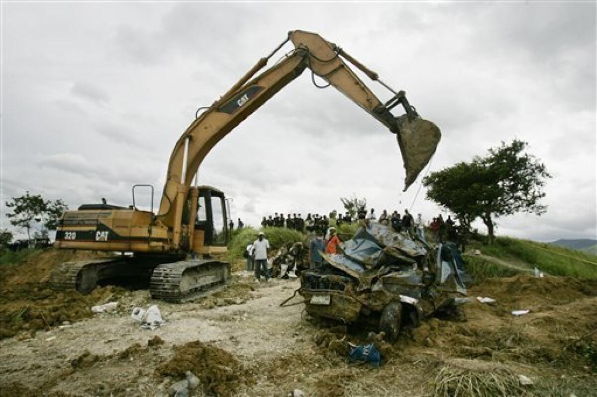FILE - In this Nov. 25, 2009 file photo, a backhoe brings down a crushed vehicle that was lifted from a hillside grave in southern Maguindanao province, Philippines. A year after 57 bodies were recovered on this grassy hilltop on Nov. 23, 2009, the body of Reynaldo Momay still remains missing. A denture dug out from the mass grave is the only trace left of Momay. (AP Photo/Aaron Favila, File)