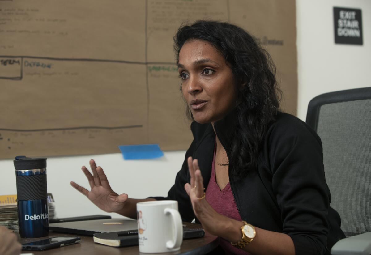 Nithya Raman holds up her hands as she sits at a desk. 