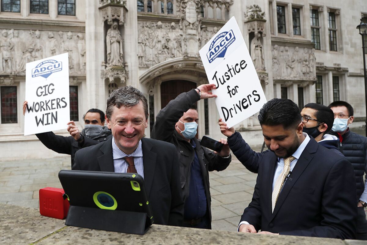 People hold "Gig Workers Win" and "Justice for Drivers" signs outside a court in London after a ruling on Uber drivers.