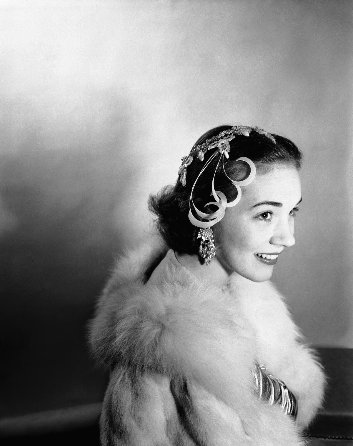 Black-and-white photo of woman in a furry shawl and a headpiece smiling
