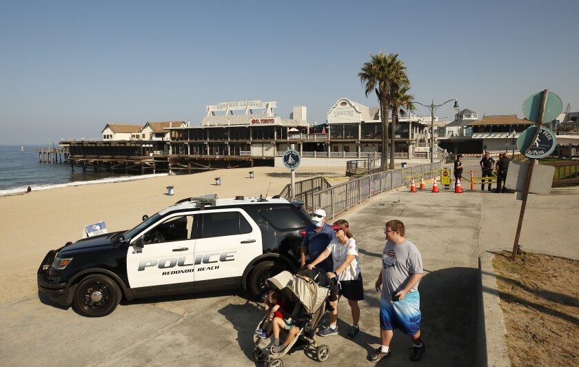 People walk past a black and white SUV with the words "Police Redondo Beach" on its doors.