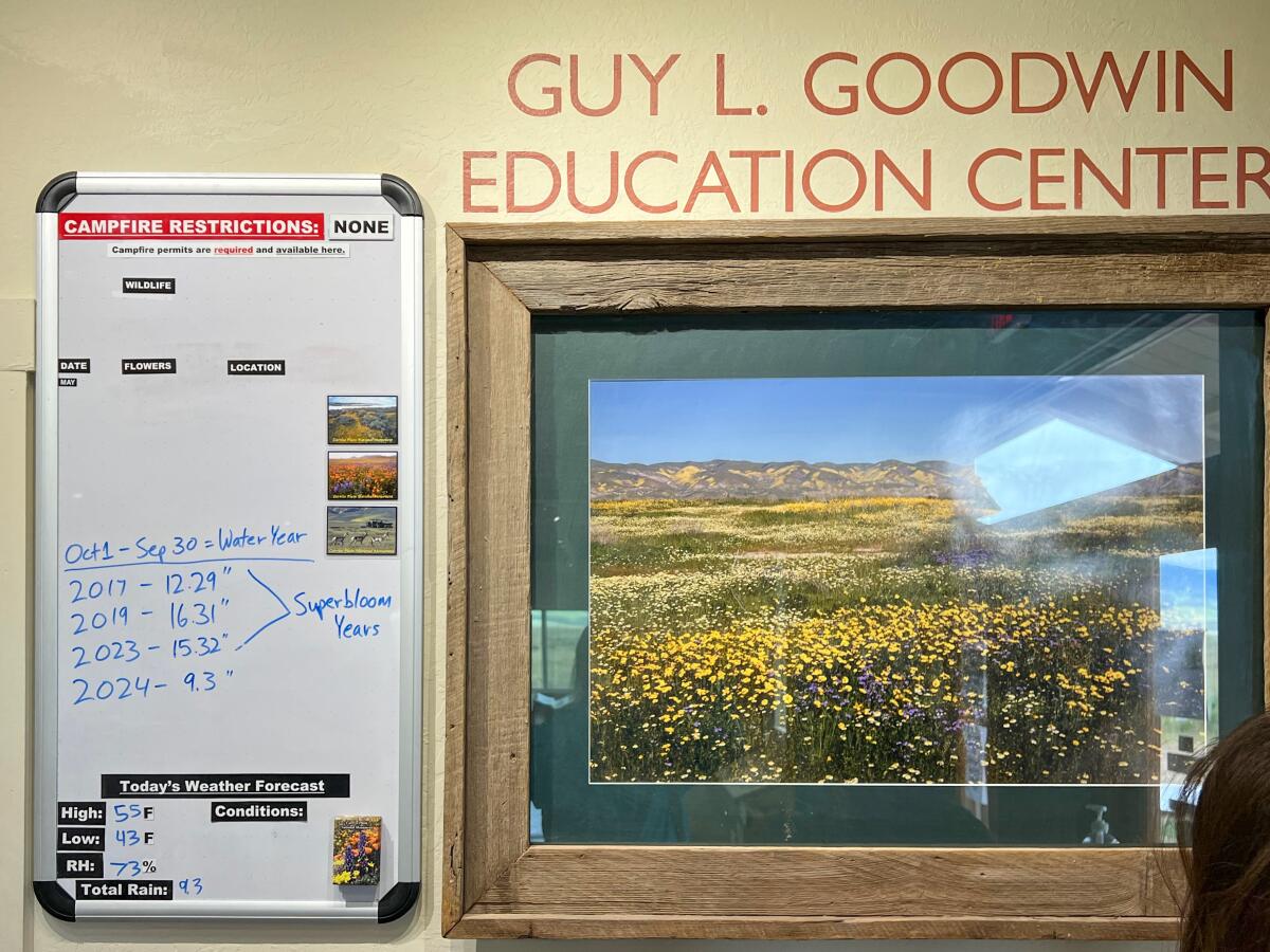 A whiteboard recording rainfall totals hangs on the wall next to framed photos of wildflowers on the plains.