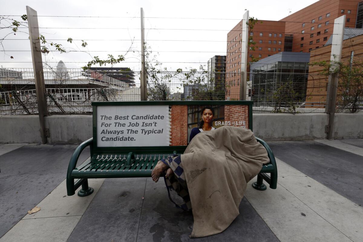 A shoeless homeless person sleep beneath a blanket on a bus bench on South Grand Avenue in Los Angeles. Julian Castro, U.S. secretary of Housing and Urban Development, is set to meet with Los Angeles officials Tuesday to discuss the issue of homelessness.