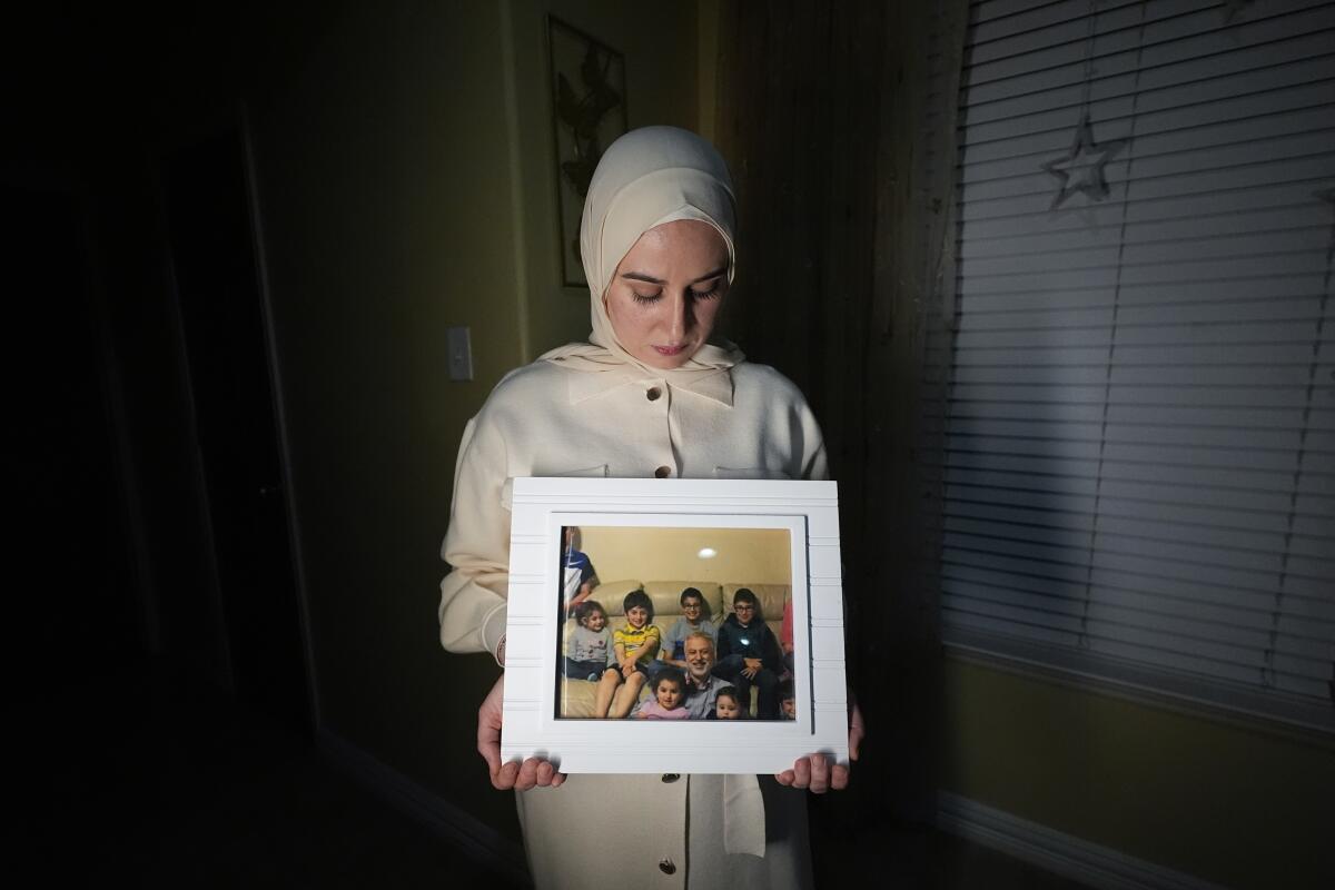 A woman holds a framed photo of a man with several of his grandchildren.
