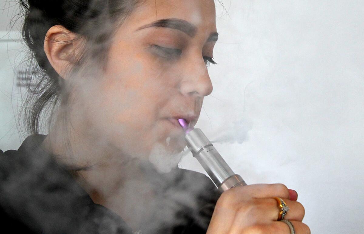 Maria Valencia uses an electronic cigarette to vaporize a nicotine solution at Vaping Ape, an e-cigarette retailer in Hollywood. The city of La Cañada Flintridge is considering prohibiting the possession of nicotine cartridges among minors, in addition to regulating the use and sale of e-cigarettes.