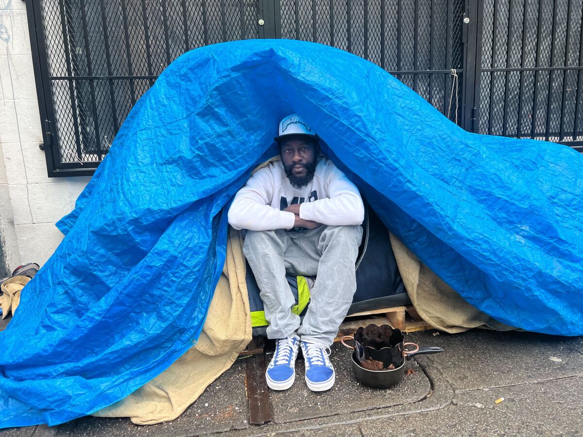 A single man sits in his tent, covered by a waterproof tarp, looking at the camera.