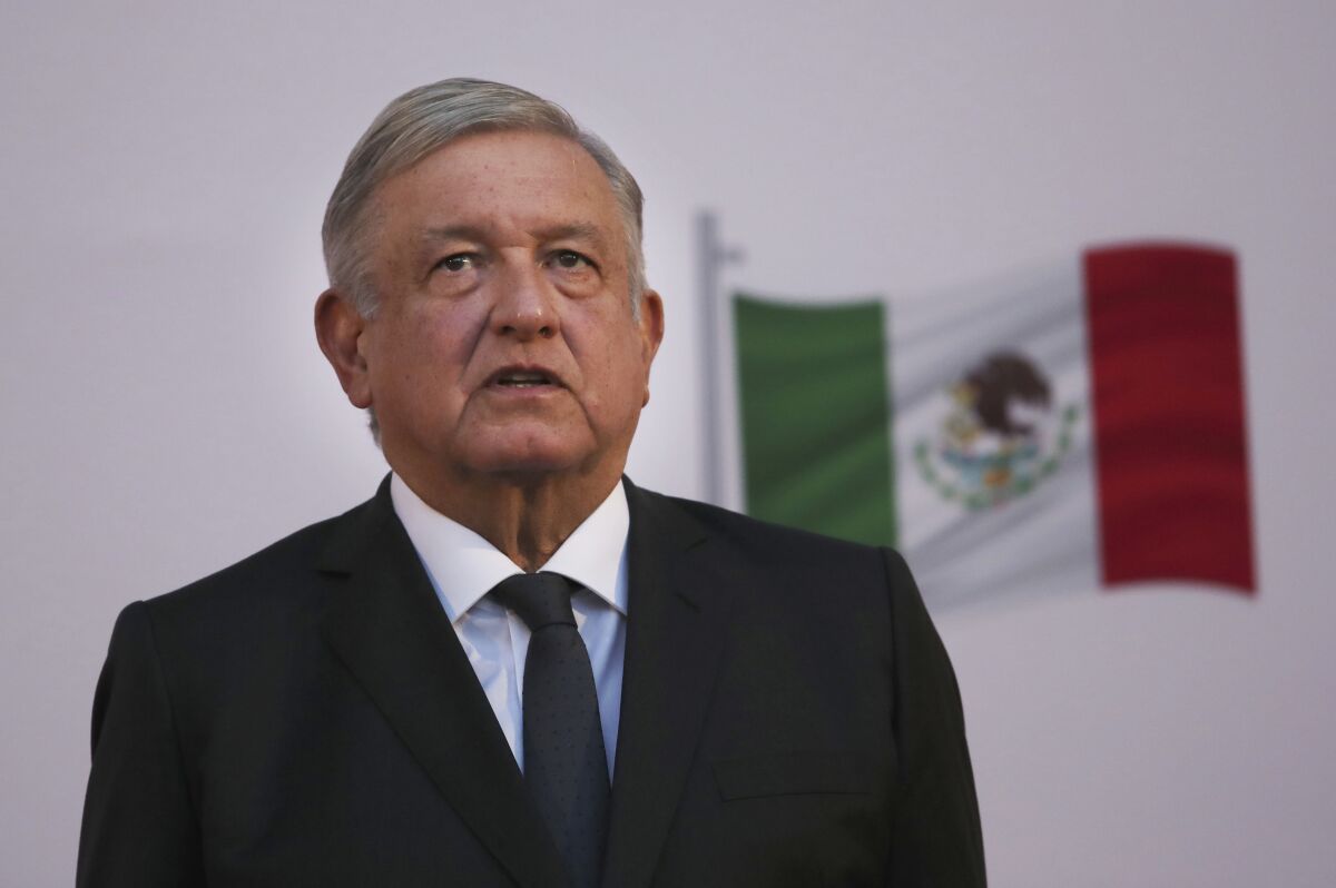 President Andrés Manuel López Obrador stands with the Mexican flag behind him.